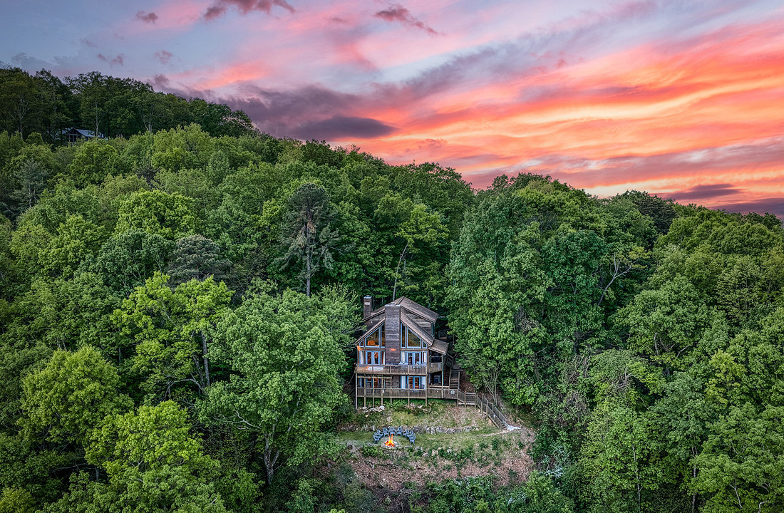 Aerial view of a cabin in the forest under a sunset sky, North Georgia cabin rental photography