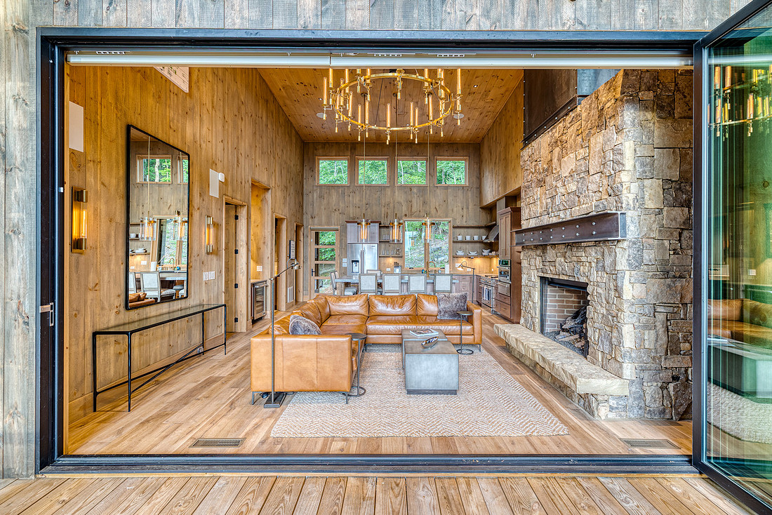 Great room of a mountain cabin with a stone fireplace and open glass wall, vacation rental interior photography